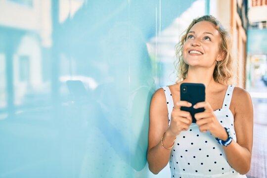 Young beautiful caucasian woman with blond hair smiling happy outdoors using smartphone