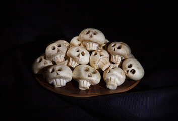 Mushrooms champignons in the form of skulls for Halloween lie in a mountain on a brown plate on a black background