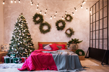 Interior of modern studio living room with comfortable bed decorated with Christmas tree and gifts