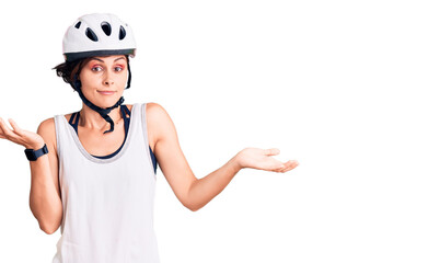 Beautiful young woman with short hair wearing bike helmet clueless and confused expression with arms and hands raised. doubt concept.