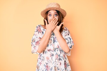 Young beautiful caucasian woman wearing summer dress and hat shocked covering mouth with hands for mistake. secret concept.