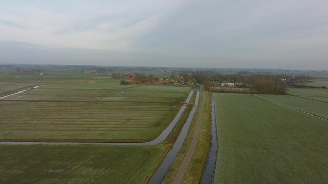 Drone Pan hover flight Over meadows to a small village in Europe The Netherlands, Friesland. Half cloudy sun in ditch and water on fields. There is some frost on the grass.