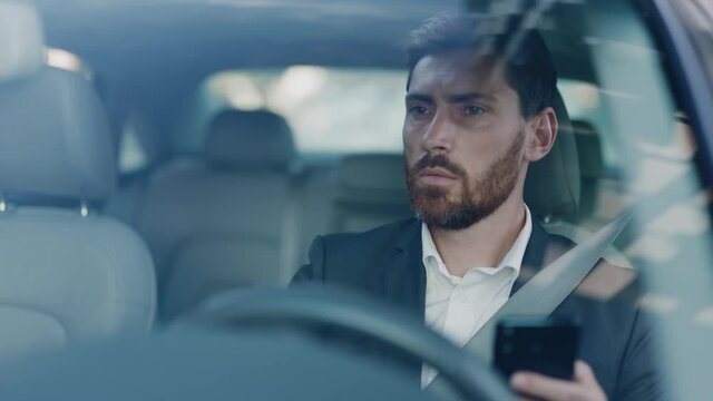 Confident focused caucasian adult businessman using smartphone application dialing colleague communicating online and driving car. Commuting. Business people lifestyle.