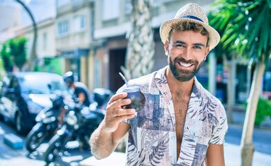 Young hispanic man on vacation smiling happy drinking mate tea at street of city