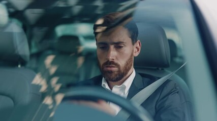 Disappointed young adult businessman waiting in traffic jam getting bored using mobile phone commuting late for work. Road adventures. City transportation. Emotions. - Powered by Adobe