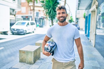 Young hispanic man smiling happy holding motorcycle helmet walking at the city
