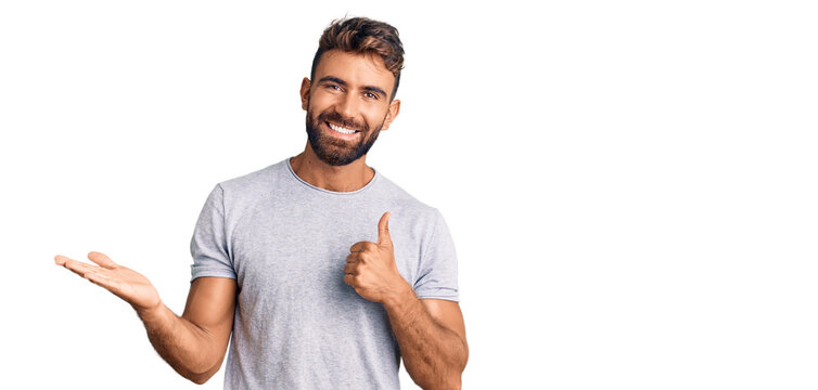 Young hispanic man wearing casual clothes showing palm hand and doing ok gesture with thumbs up, smiling happy and cheerful