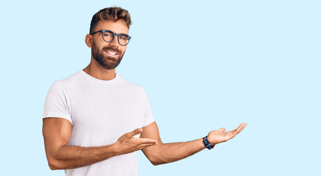 Young hispanic man wearing casual clothes and glasses inviting to enter smiling natural with open hand