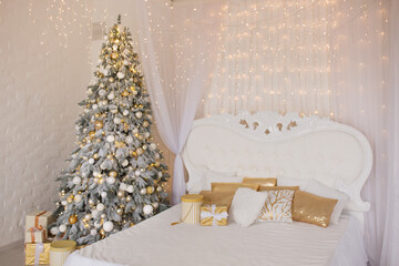 A spacious white light bedroom with a decorated Christmas tree and a garland. New Year interior