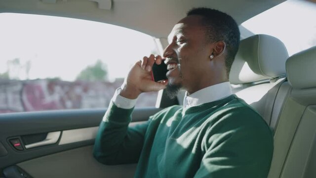 Successful afro-american confident businessman speaking mobile phone conversation explaining to business partner commuting to work in private luxury taxi transportation.