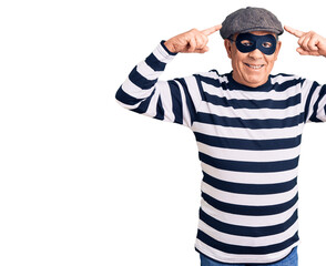 Senior handsome man wearing burglar mask and t-shirt smiling pointing to head with both hands finger, great idea or thought, good memory