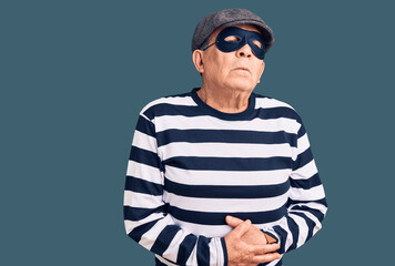 Senior handsome man wearing burglar mask and t-shirt with hand on stomach because indigestion, painful illness feeling unwell. ache concept.