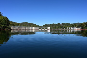 Fototapeta premium Santeetlah Dam on Lake Santeetlah and Cheoah River in Graham County, North Carolina reflected in calm water of lake on clear autumn afternoon.