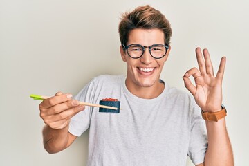 Handsome caucasian man eating sushi using chopsticks doing ok sign with fingers, smiling friendly gesturing excellent symbol