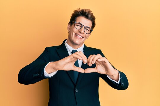 Handsome caucasian man wearing business suit and tie smiling in love doing heart symbol shape with hands. romantic concept.