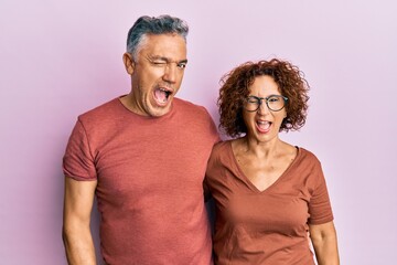 Beautiful middle age couple together wearing casual clothes winking looking at the camera with sexy expression, cheerful and happy face.