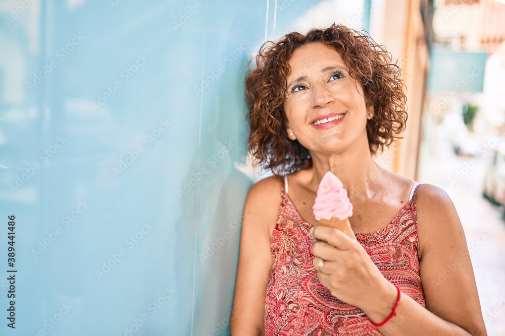 Wall mural Middle age woman eating ice cream leaning on the wall at street of city.