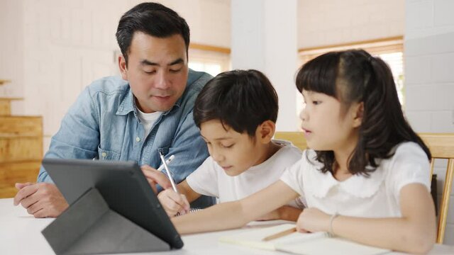 Happy Asia family homeschooling, father teach children using digital tablet in living room at home. Spending time together, Self-isolation, Social distancing, Quarantine for corona virus prevention.