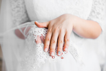 Wedding manicure on the background of a lace veil. Hands of the bride with a delicate manicure in beige and white shades with a blue pattern. Image with selective focus and tinting.