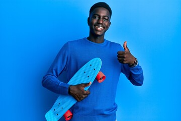 Young african american man holding skate smiling happy and positive, thumb up doing excellent and approval sign