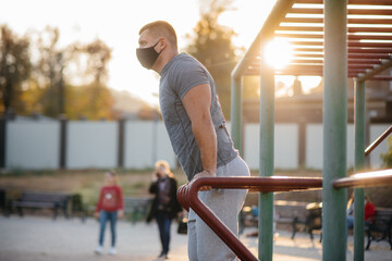 A young man does push-UPS, pull-UPS on a sports field in a mask during a pandemic at sunset. Sports, healthy lifestyle