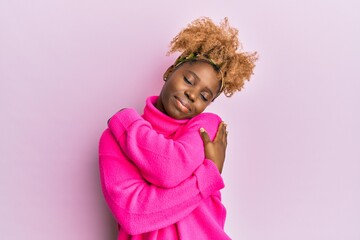 Young african woman with afro hair wearing casual winter sweater hugging oneself happy and positive, smiling confident. self love and self care