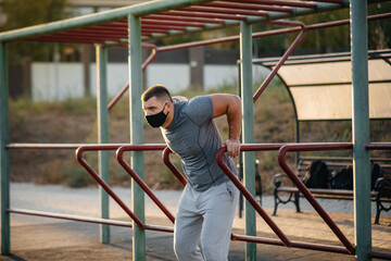 A young man does push-UPS, pull-UPS on a sports field in a mask during a pandemic at sunset. Sports, healthy lifestyle