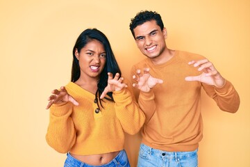 Beautiful latin young couple wearing casual clothes together smiling funny doing claw gesture as cat, aggressive and sexy expression