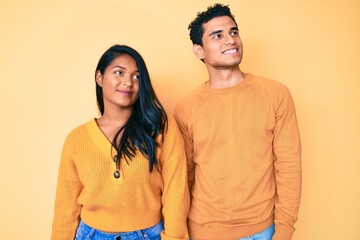 Beautiful latin young couple wearing casual clothes together smiling looking to the side and staring away thinking.