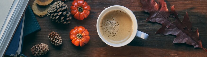 Cup of coffee on wooden table with book and autumn decorations. Wide composition.