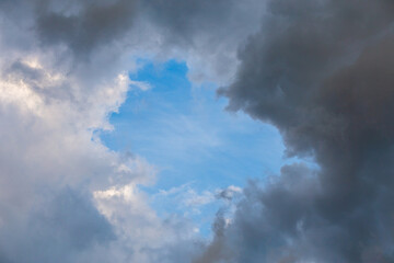 natural blue sky window in clouds, round gap in solid summer clouds