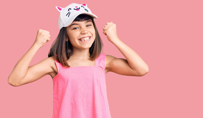 Young little girl with bang wearing funny kitty cap screaming proud, celebrating victory and success very excited with raised arms
