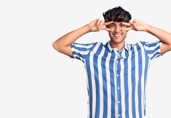 Young hispanic man wearing casual clothes doing peace symbol with fingers over face, smiling cheerful showing victory