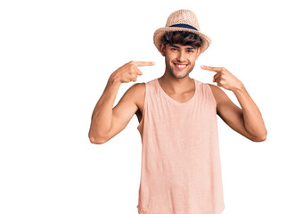 Young hispanic man wearing summer hat smiling cheerful showing and pointing with fingers teeth and mouth. dental health concept.