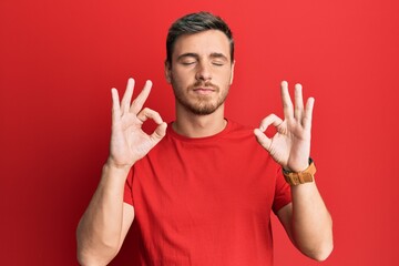 Handsome caucasian man wearing casual red tshirt relaxed and smiling with eyes closed doing meditation gesture with fingers. yoga concept.