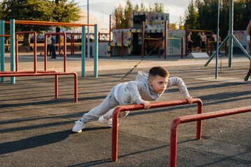 Fototapeta premium A little boy doing push-UPS on the Playground during sunset. Sports, healthy lifestyle