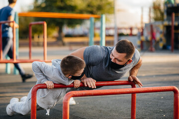 Obraz premium Father and son play sports on the sports field in masks during sunset. Healthy parenting and healthy lifestyle