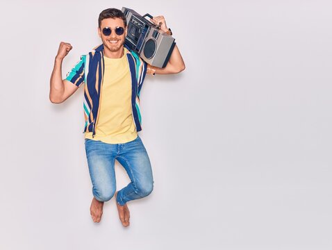 Young handsome hispanic man wearing sunglasses smiling happy. Jumping with smile on face celebrating with fist raised over isolated white background