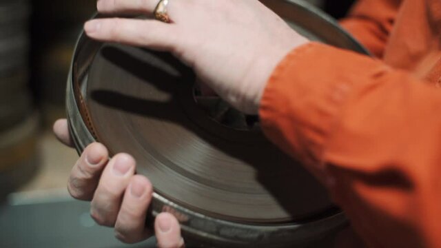 Metal box with film tape in the hands of a man who closes it and returns it to the shelf at other metal boxes