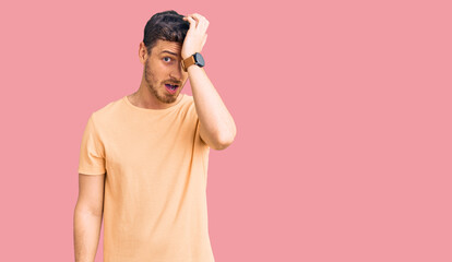 Handsome young man with bear wearing casual yellow tshirt surprised with hand on head for mistake,...