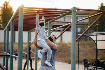 Obraz premium Father and son play sports on the sports field in masks during sunset. Healthy parenting and healthy lifestyle