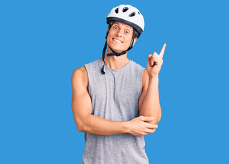 Young handsome man wearing bike helmet with a big smile on face, pointing with hand and finger to the side looking at the camera.