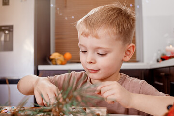 Little boy painting gingerbread man. Handmade Christmas gift ideas. Kitchen decorated for Christmas. Horizontal shot.