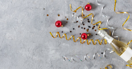 New Year background with golden champagne bottle, confetti stars and party serpentine top view on grey table.