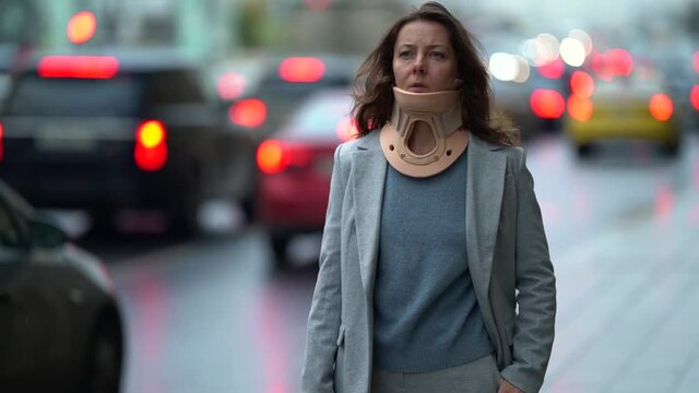 injured woman with cervical collar is waiting taxi in city, standing near road with many of auto