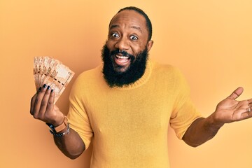 Young african american man holding south african 20 rand banknotes celebrating achievement with happy smile and winner expression with raised hand