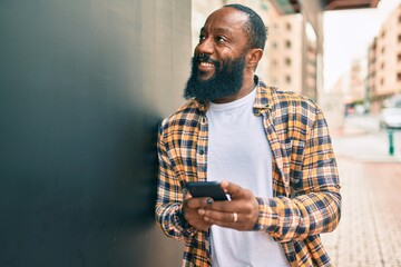 African american man with beard using smartphone typing and texting at the street with a happy smile