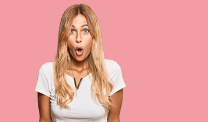 Beautiful blonde young woman wearing casual white tshirt afraid and shocked with surprise...