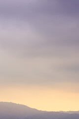 Silhueta de serra distante com céu ao entardecer mesclando tons de rosa, amarelo e púrpura, em estilo minimalista, quase abstrato.