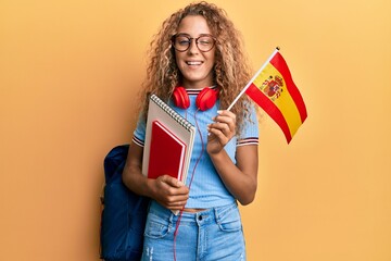 Beautiful caucasian teenager girl exchange student holding spanish flag winking looking at the...